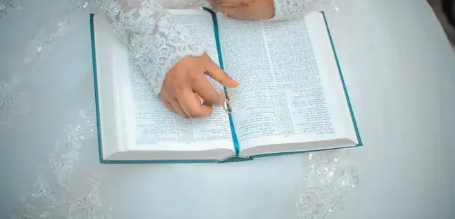 Photo of an on open Bible with a lady's hand placed on top it