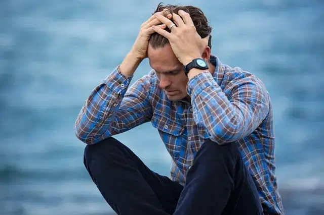Man in Blue and Brown Plaid Dress Shirt Touching His Hair in a worry posture